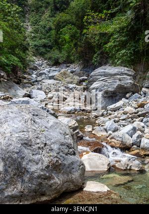 Letto del fiume Sanzhanxi con grandi massi nel Parco Nazionale di Taroko. La lussureggiante foresta verde copre pendii ripidi. Un piccolo torrente scorre attraverso le rocce. Foto Stock
