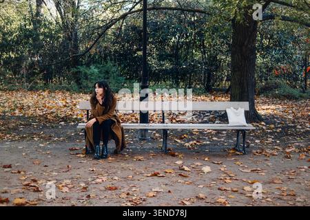 In autunno, la donna siede con cura sulla panchina del parco con una borsa bianca accanto a lei. Affrontare lo stress, la riflessione emotiva sulla salute, gestire l'ansia Foto Stock