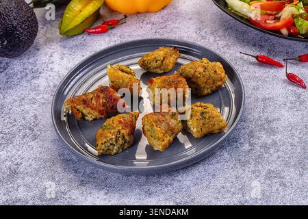 Peperoncini di pollo fritti croccanti su un piatto di ceramica grigia con peperoncino rosso, avocado e insalata fresca sullo sfondo Foto Stock