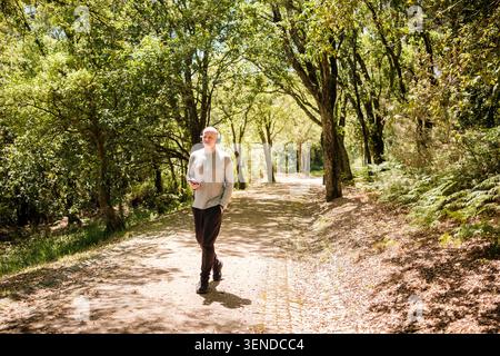 Uomo che ama passeggiare nella foresta, tenendo il telefono cellulare e indossando le cuffie Foto Stock