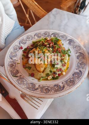 Bistecca di cavolfiore arrosto con salsa alle erbe verdi, noci tostate e semi di melograno su un piatto decorativo vintage, fotografata in un caffè in marmo Foto Stock