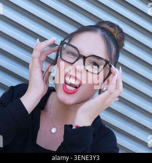 Ritratto ravvicinato di una giovane donna caucasica ventenne che indossa eleganti occhiali da vista rotondi. Sorride e gesta allegramente. Foto Stock