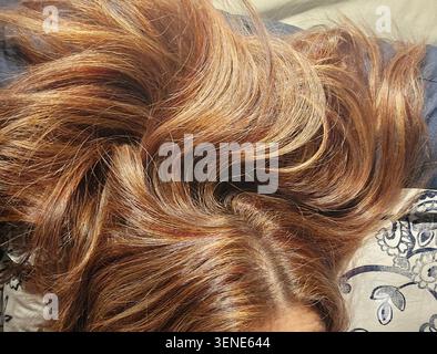 Primo piano dettagliato che si concentra su capelli marroni multicolore, lunghi e ondulati con particolari dettagli biondi e caramello, spalmati naturalmente su un letto con Foto Stock