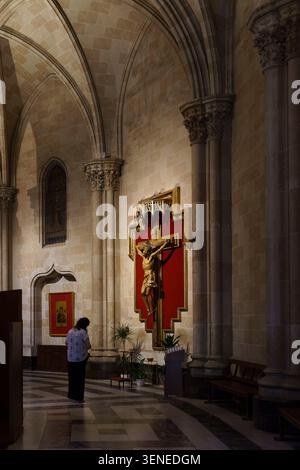 Una donna sta in preghiera davanti a un grande crocifisso su sfondo rosso all'interno della basilica di San Vicente Ferrer a Valencia in Spagna Foto Stock