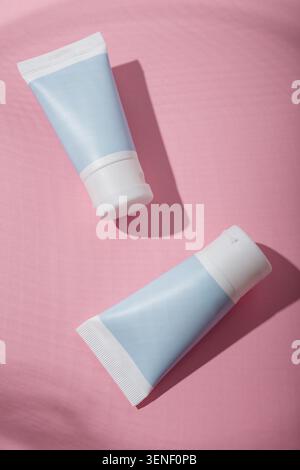Due tubi blu per cosmetici senza marchio, mockup su sfondo rosa, luce intensa con ombre. Modello di prodotti di bellezza, banner pubblicitario. Copia spazio Foto Stock