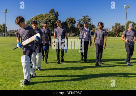 Diversi giocatori di cricket maschili che camminano sull'erba esterna indossando camicie grigie con pistrelli Foto Stock