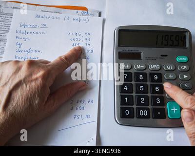 Kirov, Russia - 18 marzo 2026: Calcolo delle spese mensili a casa con una calcolatrice e documenti sul tavolo durante le ore serali. Foto Stock