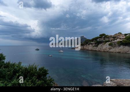 Barche a vela ancorate in una baia cristallina con acque turchesi e costa di montagna Foto Stock