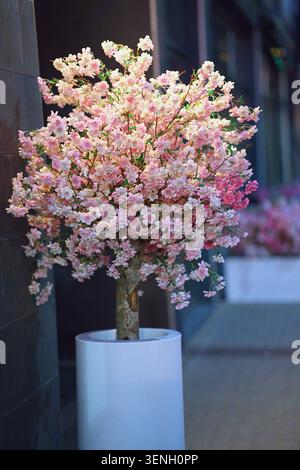 Un albero artificiale in fiore di ciliegio realizzato in tessuto e materiali sintetici per simulare i fiori di ciliegio selvatici. Foto verticale Foto Stock