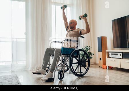 visuale a tutta lunghezza dell'uomo determinato su sedia a rotelle che solleva manubri verdi durante l'allenamento con pressa a soffitto luminoso soggiorno che rappresenta gli adattamenti Foto Stock