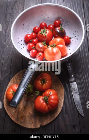 Pomodori ciliegini in colino con coltello, stile rustico. Verdure fresche lavate, preparazione per la cucina casalinga Foto Stock