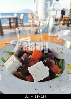 Cibo autentico con insalata greca fresca e vino al crepuscolo in una taverna sul porto. Foto di scorta della cucina greca di alta qualità per blog culinari. Foto Stock