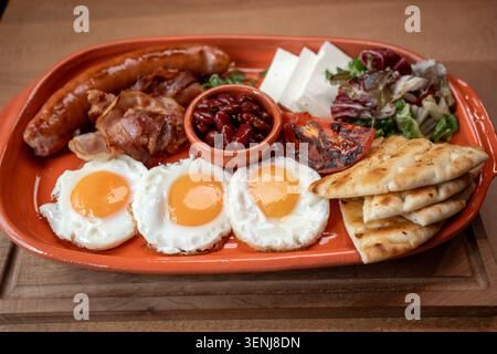 Il piatto della colazione comprende uova, salsiccia, pancetta e verdure fresche Foto Stock