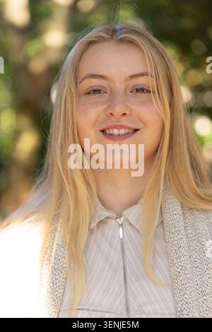 Donna ventenne in piedi nel parco, indossa una camicia a righe con zip frontale e cardigan in maglia Foto Stock