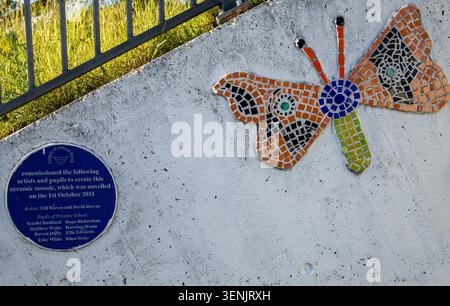 Un colorato mosaico decorativo a farfalla realizzato con piastrelle di ceramica su una parete di cemento accanto a una targa commemorativa Calne Wiltshire Foto Stock