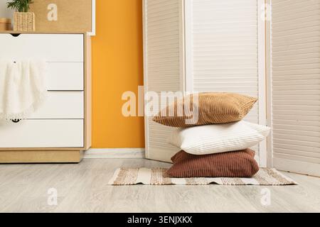 Interni accoglienti con cuscini in velluto a coste sovrapposti su un tappeto a righe, arredi moderni e minimalisti e una calda parete arancione Foto Stock