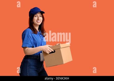 Giovane donna sorridente in uniforme blu con scatola di cartone, shopping online e servizio di spedizione veloce, logistica affidabile e soddisfazione del cliente Foto Stock