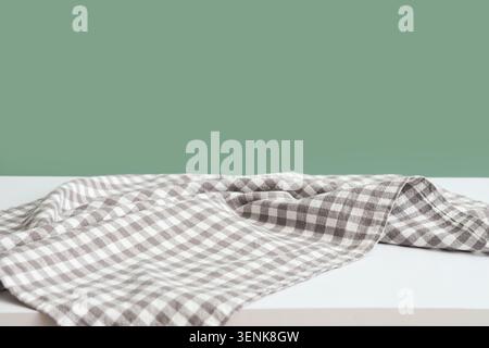 Tessuto a scacchi di colore Vichy su tavolo bianco con sfondo verde, spazio vuoto per l'esposizione dei prodotti e la fotografia di cibo, lo sfondo verde offre un'atmosfera unica Foto Stock
