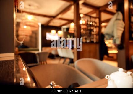 Interni caldi del ristorante con sfondo sfocato, accogliente atmosfera da caffetteria, tavoli e sedie vuoti, illuminazione soffusa Foto Stock