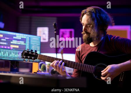Musicista esperto che suona la chitarra acustica e registra nuovi brani da utilizzare per mixare e padroneggiare le tecniche in casa, con la composizione di musica moderna con software per workstation audio digitale e apparecchiature audio. Foto Stock