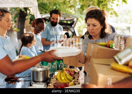 Il gruppo multirazziale offre assistenza distribuendo cibo ai poveri e ai bisognosi, volontari di diverse etnie si uniscono per aiutare i senzatetto partecipando a iniziative umanitarie di aiuto alimentare. Foto Stock