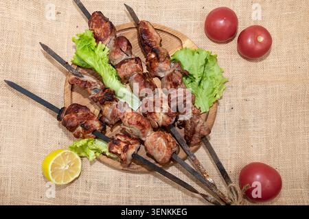 Spiedini di shashlik di maiale grigliati serviti con pomodori con lattuga fresca e limone su tavola di legno rustico Foto Stock