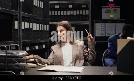 Sul telefono fisso, una donna delle forze dell'ordine riceve informazioni critiche e fornisce nuovi indizi sui casi alla poliziotta afroamericana. Nella sala degli incidenti, investigatore privato caucasico su chiamata. Foto Stock