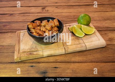 Primo piano di natura morta con pancetta di maiale brasiliana scoppiettante con zeppe di lime fresche su tavola rustica di legno, con una calda luce dorata. Perfetto f Foto Stock