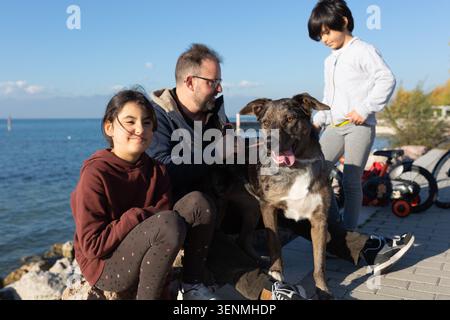 La famiglia si diverte con il cane sul lungolago nelle giornate di sole Foto Stock