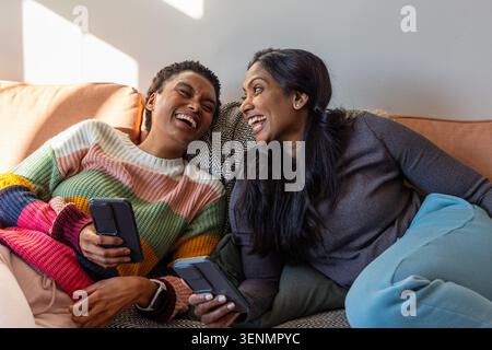 Diverse amiche si sdraiano sul divano di casa, indossano un maglione a righe e tengono in mano i telefoni Foto Stock