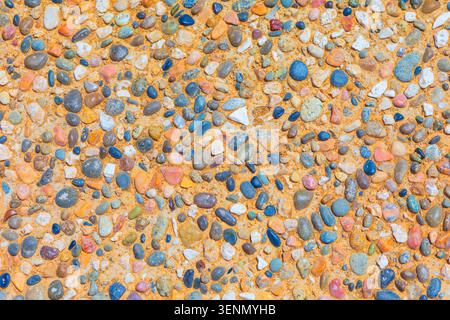 Ciottoli colorati incorporati in una terra sabbiosa, che creano un vivace mosaico. Pietre di varie forme e dimensioni formano un motivo ricco e naturale Foto Stock