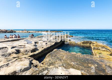 Sliema, Malta - 16 maggio 2025: Persone che si rilassano presso la costa rocciosa delle terme romane a Sliema, Malta, godendosi il sole, il turchese wat del Mediterraneo Foto Stock