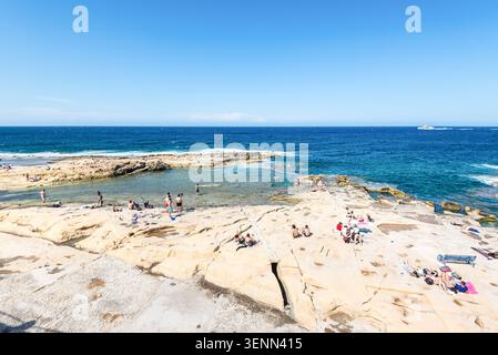 Sliema, Malta - 16 maggio 2025: Persone che si rilassano presso la costa rocciosa delle terme romane a Sliema, Malta, godendosi il sole, il turchese wat del Mediterraneo Foto Stock