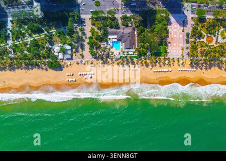 Vista dall'alto di una spiaggia sabbiosa con ombrelloni e lettini, con un parco sull'argine e caffetterie lungo la città. Foto Stock