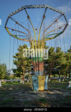 Un vecchio giro in giostra, abbandonato, si erge abbandonato in un parco divertimenti dimenticato, con la sua colorata vernice sbiadita e l'arrugginimento dei metalli. Intorno a t Foto Stock