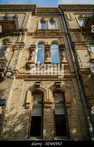 Questa vista dall'alto dall'angolo basso cattura l'architettura dettagliata di un vecchio edificio a più piani in mattoni gialli a Batumi, Georgia, caratterizzato da finestre ad arco Foto Stock