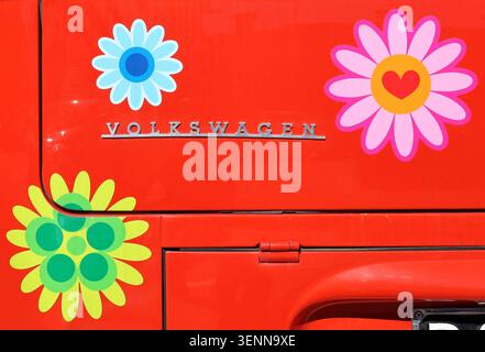 Udine, Italia. 24 marzo 2024 logo Volkswagen con adesivi decorativi sul retro di un VW Transporter rosso vintage tipo 2. Foto Stock