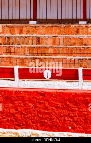 Composizione grafica dell'interno dell'arena, con la barriera in pietra verniciata di rosso brillante, un pennarello bianco con numero uno e file di bri rustico Foto Stock