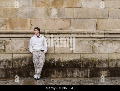 Giovane uomo premuroso appoggiato a un vecchio muro di pietra Foto Stock