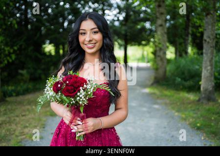 Giovane donna felice in abito rosso con bouquet di rose Foto Stock
