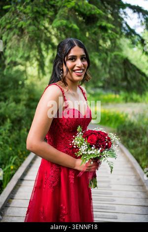 Giovane donna sorridente in abito rosso con bouquet di fiori Foto Stock
