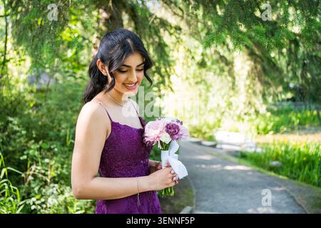 Giovane donna felice con un vestito viola che tiene fiori Foto Stock