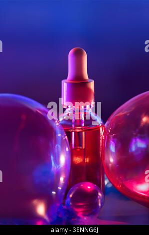 Il flacone contagocce in vetro contenente siero rosa è posizionato tra sfere traslucide, illuminate da effetti di luce blu e viola sullo sfondo Foto Stock