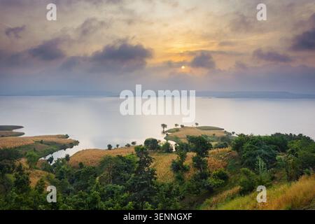 Un'alba mozzafiato illumina il cielo su un lago tranquillo e un vivace paesaggio verde a Banswara, Rajasthan, India. Foto Stock