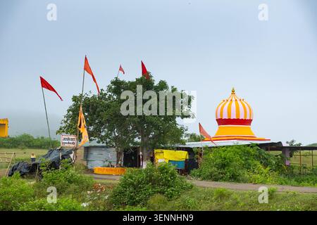 Una variopinta cupola del tempio e bandiere di preghiera sventolanti si stagliano in mezzo alla vegetazione lussureggiante del Rajasthan rurale, in India. Foto Stock