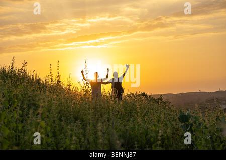 Sagome di due persone con le braccia alzate in trionfo contro un vibrante tramonto dorato. Foto Stock