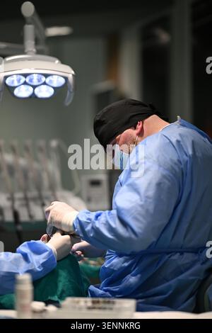 Dentista maschile che esegue chirurgia dentale in clinica indossando maschera chirurgica e copertura per la testa Foto Stock