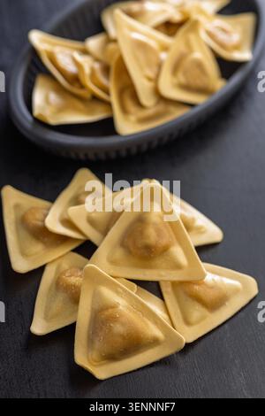 Primo piano di ravioli triangolari su una superficie di legno scuro, evidenziando la pasta ripiena cruda con impasto dorato. Ideale per la cucina italiana, le immagini delle ricette, lo styling del cibo e il contenuto culinario o il design del menu. Foto Stock