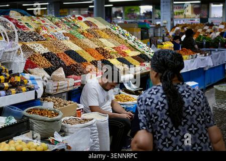 Almaty, Kazakistan - giugno 2026: Un venditore tende a un mercato pieno di frutta secca, noci e semi presso il Green Bazaar di Almaty, Kazakistan. Foto Stock