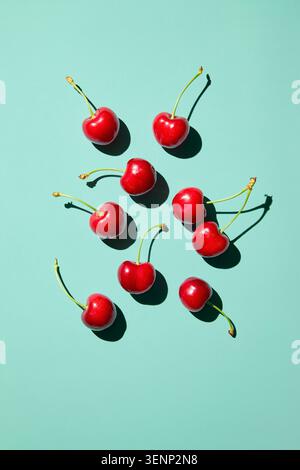 Ciliegie dolci mature disposte su sfondo turchese con ombre alla luce del sole, vista dall'alto Foto Stock